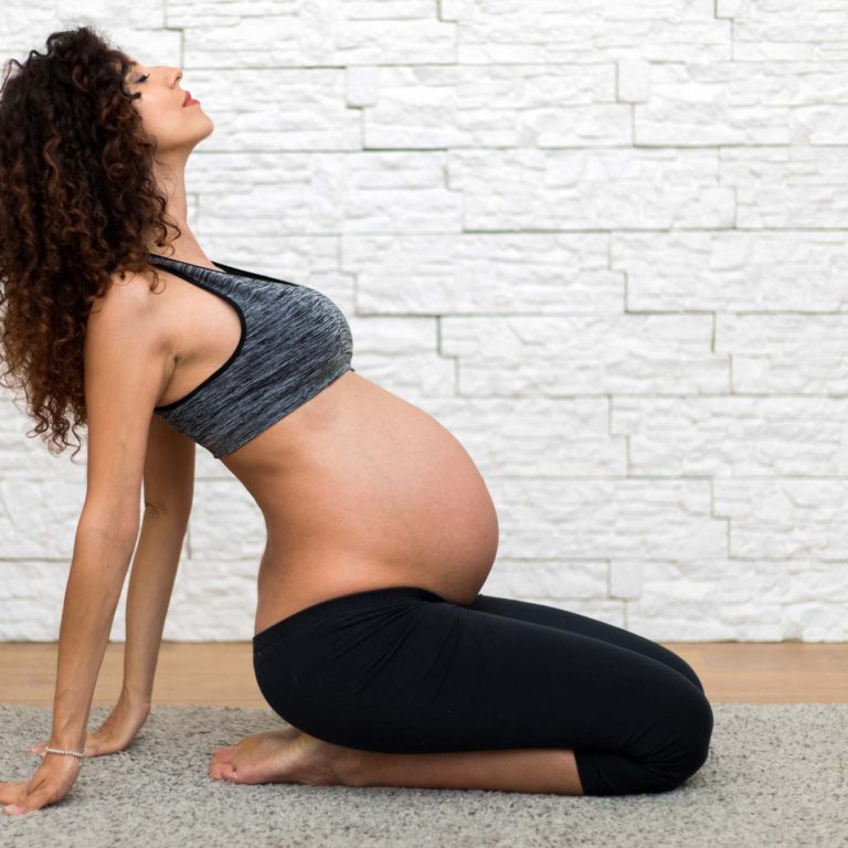 Pregnant person on their knees leans backward in a stretching posture