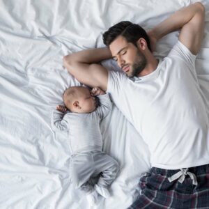Young baby and parent both sleeping on their backs leaning in toward each other